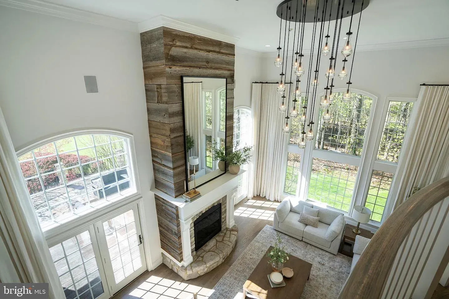 Bright living room with fireplace, tall windows, and a hanging beaded chandelier overlooking a garden.
