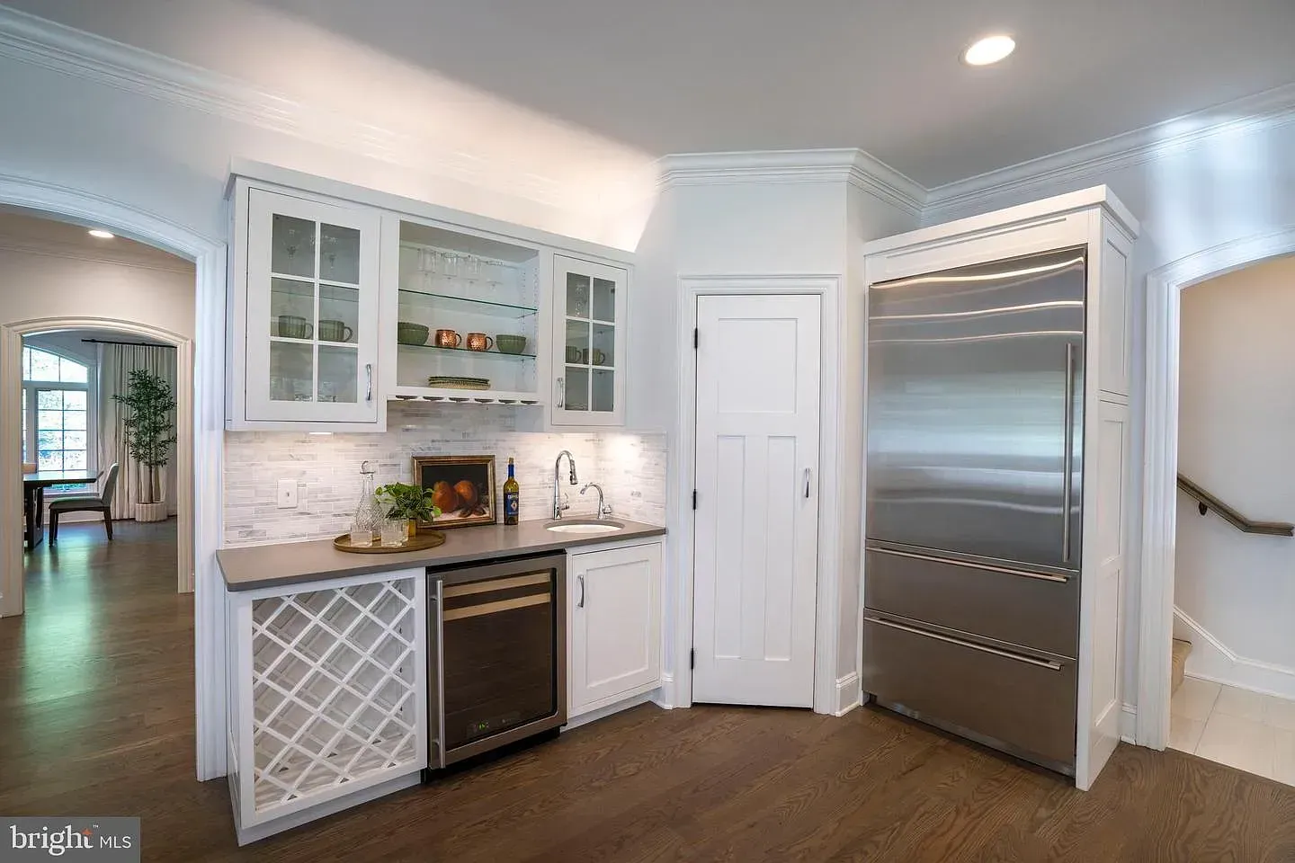 Modern kitchen with white cabinets, stainless steel fridge, wine rack, and dark wood floor