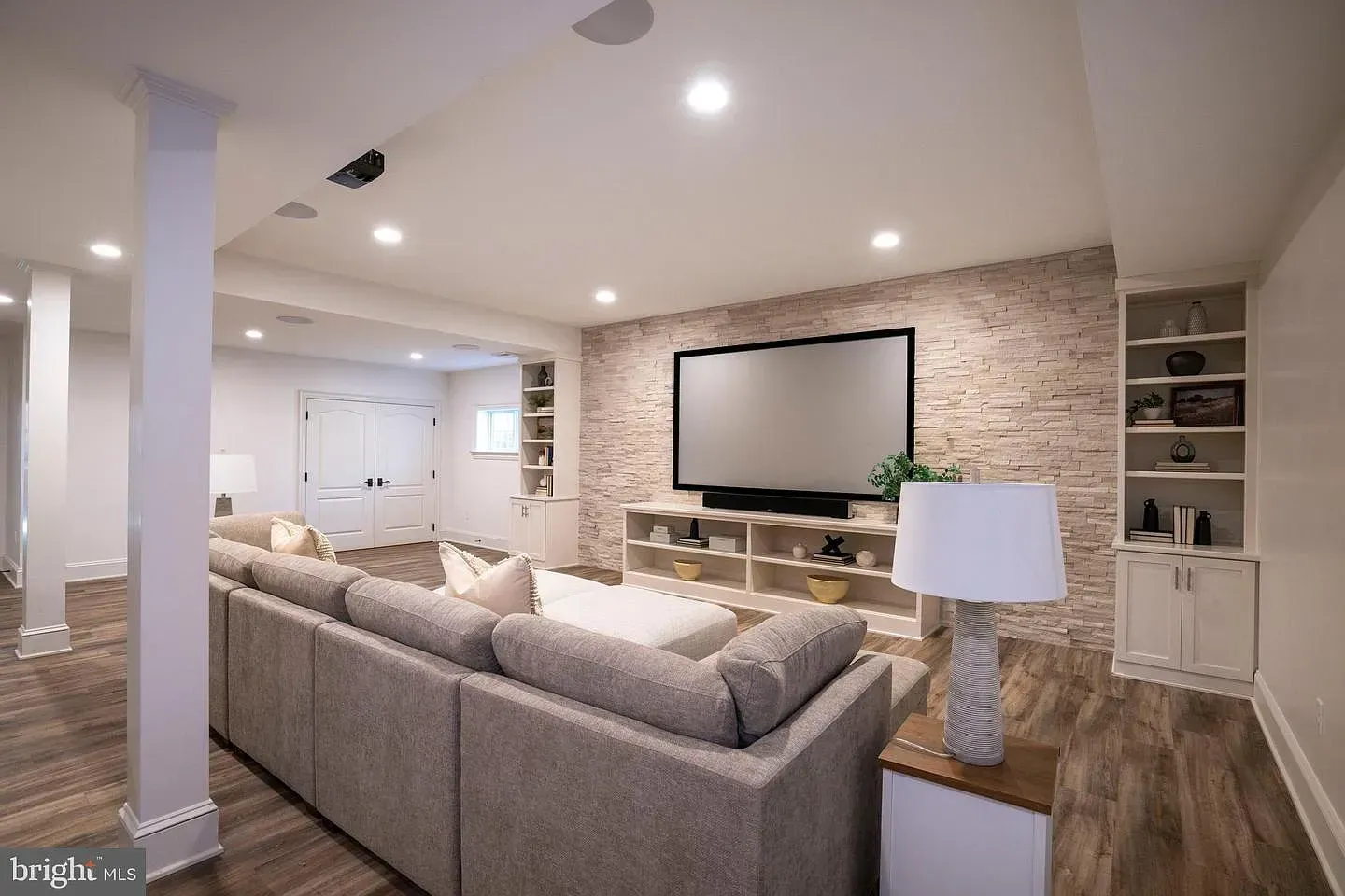 Spacious modern basement living room with beige sectional, brick accent wall, and wall-mounted TV