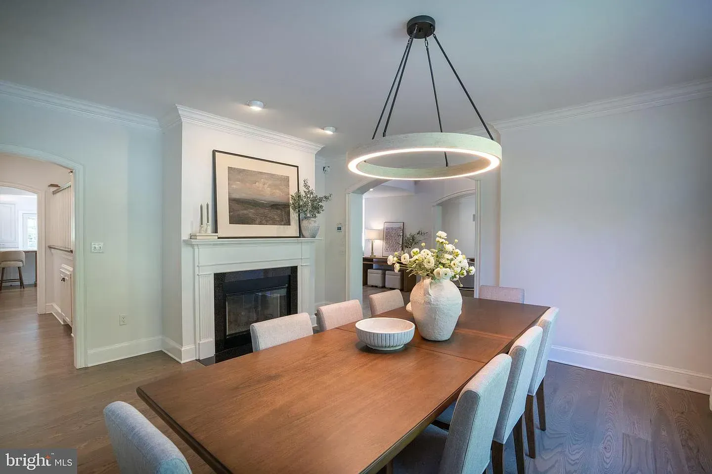 Elegant dining room with wooden table, white chairs, fireplace, and modern ring chandelier