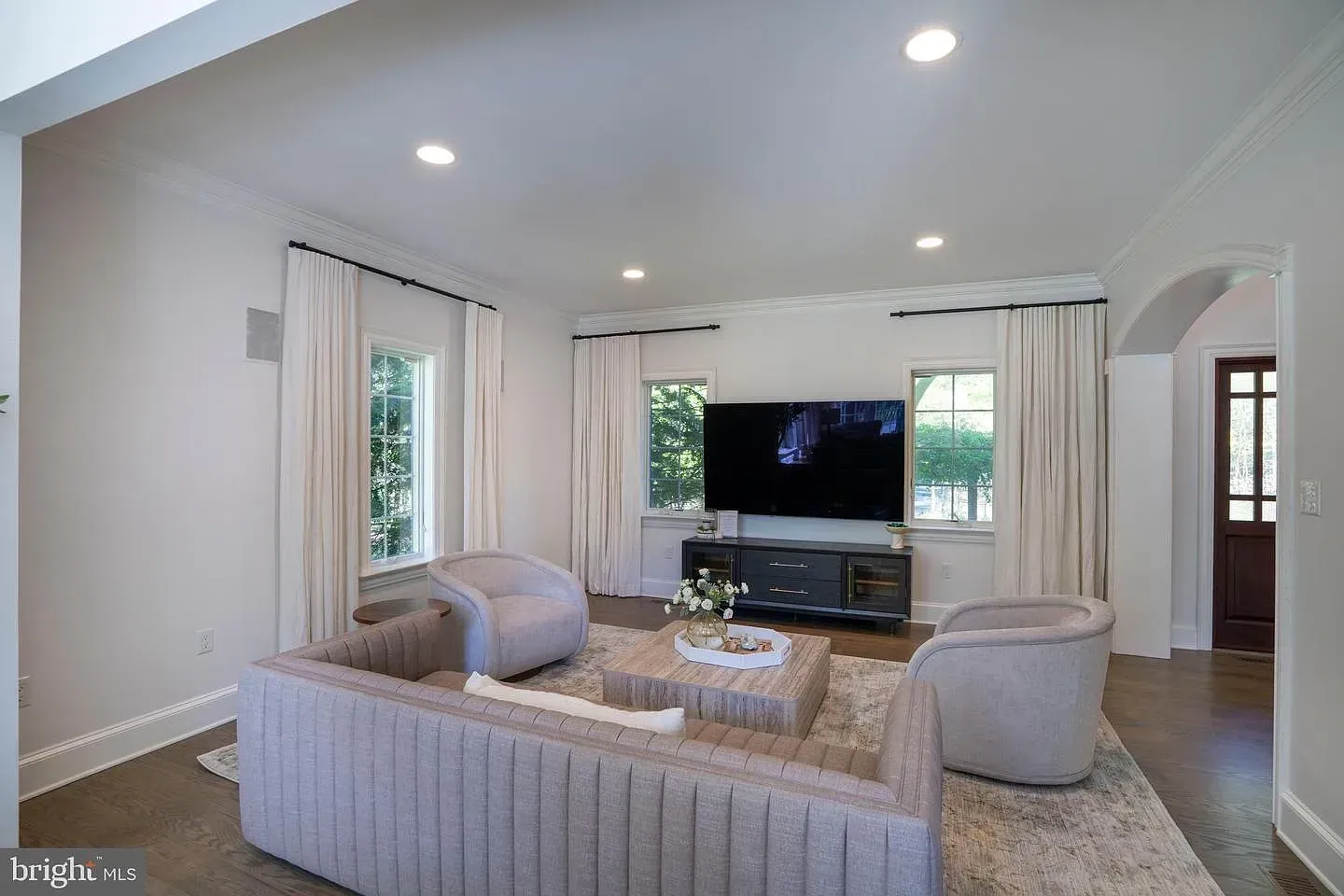 Bright living room with gray sectional, wall-mounted TV, round chairs, and large windows