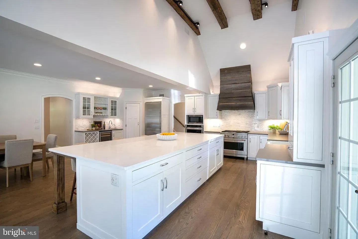 Bright white kitchen with large island, wood ceiling beams, and stainless steel appliances