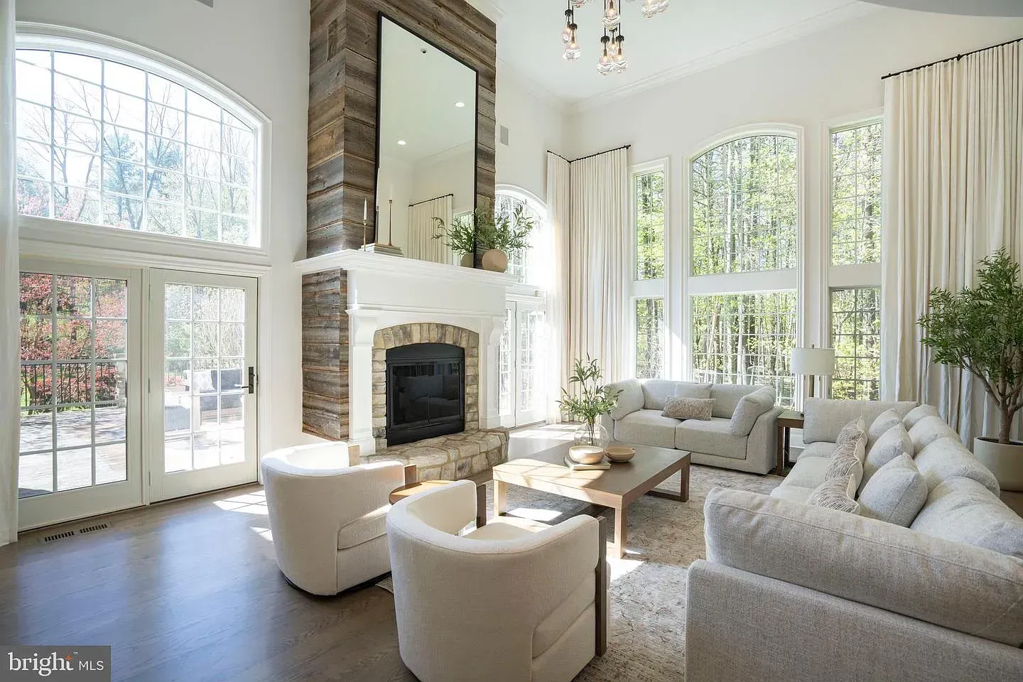 Bright living room with tall windows, white fireplace, and light-colored sofas and chairs