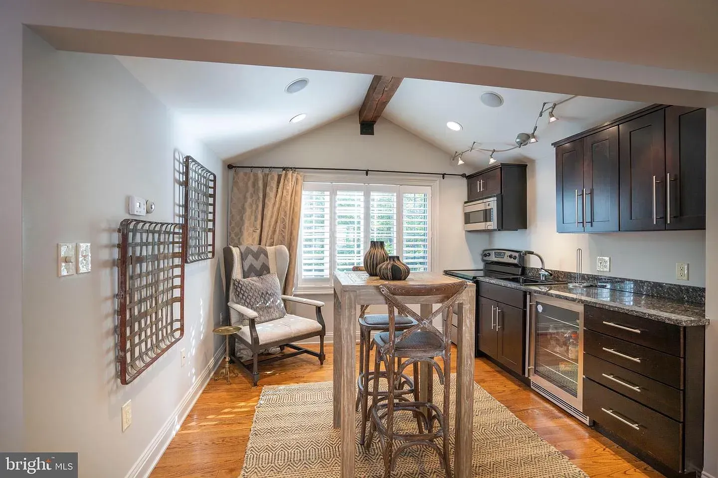 Bright kitchen and dining nook with granite counters, barstools, patterned rug, and a chair by the window.