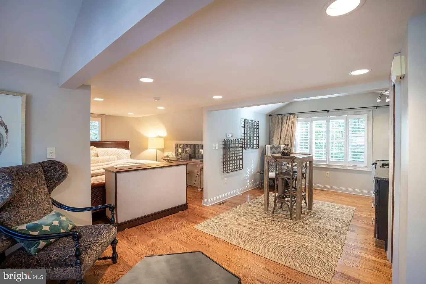 Open living and dining area with hardwood floors, white kitchen, rug, and window seat under slanted ceiling