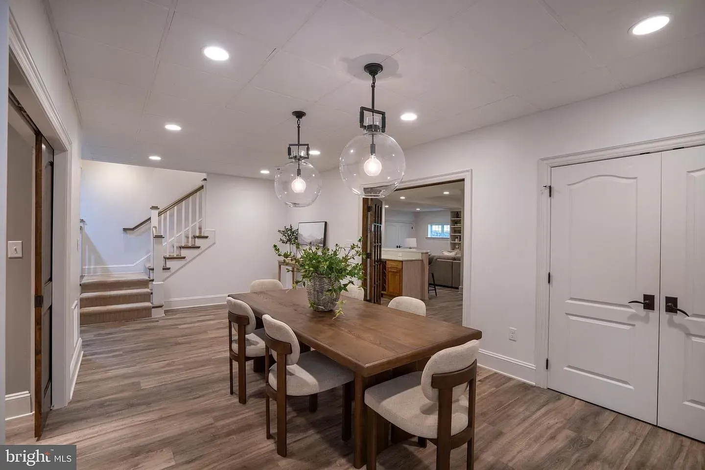 Bright dining room with wood table, pendant lights, staircase, and white double doors