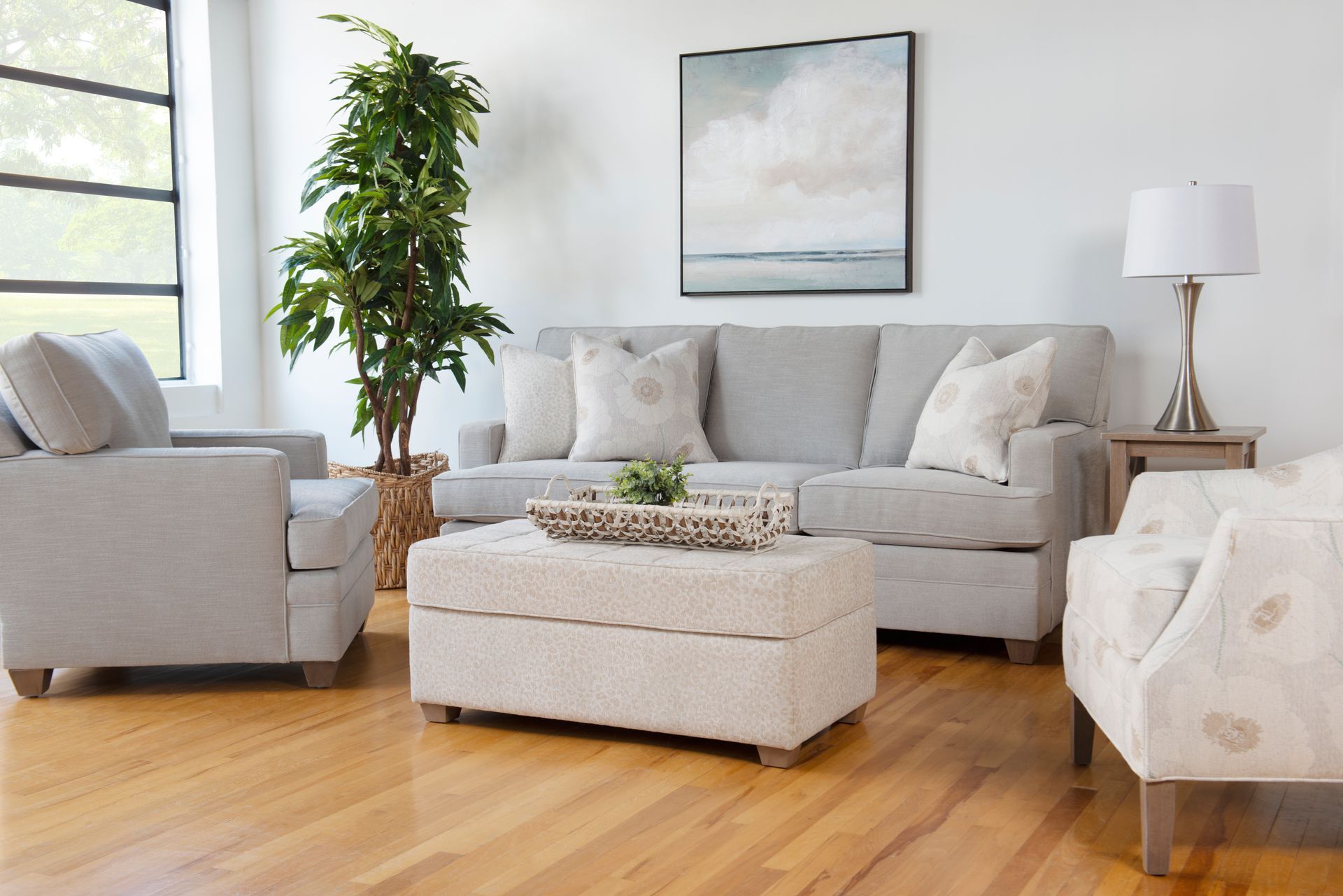 Bright modern living room with a light sofa, ottoman, armchair, plant, and wooden floor