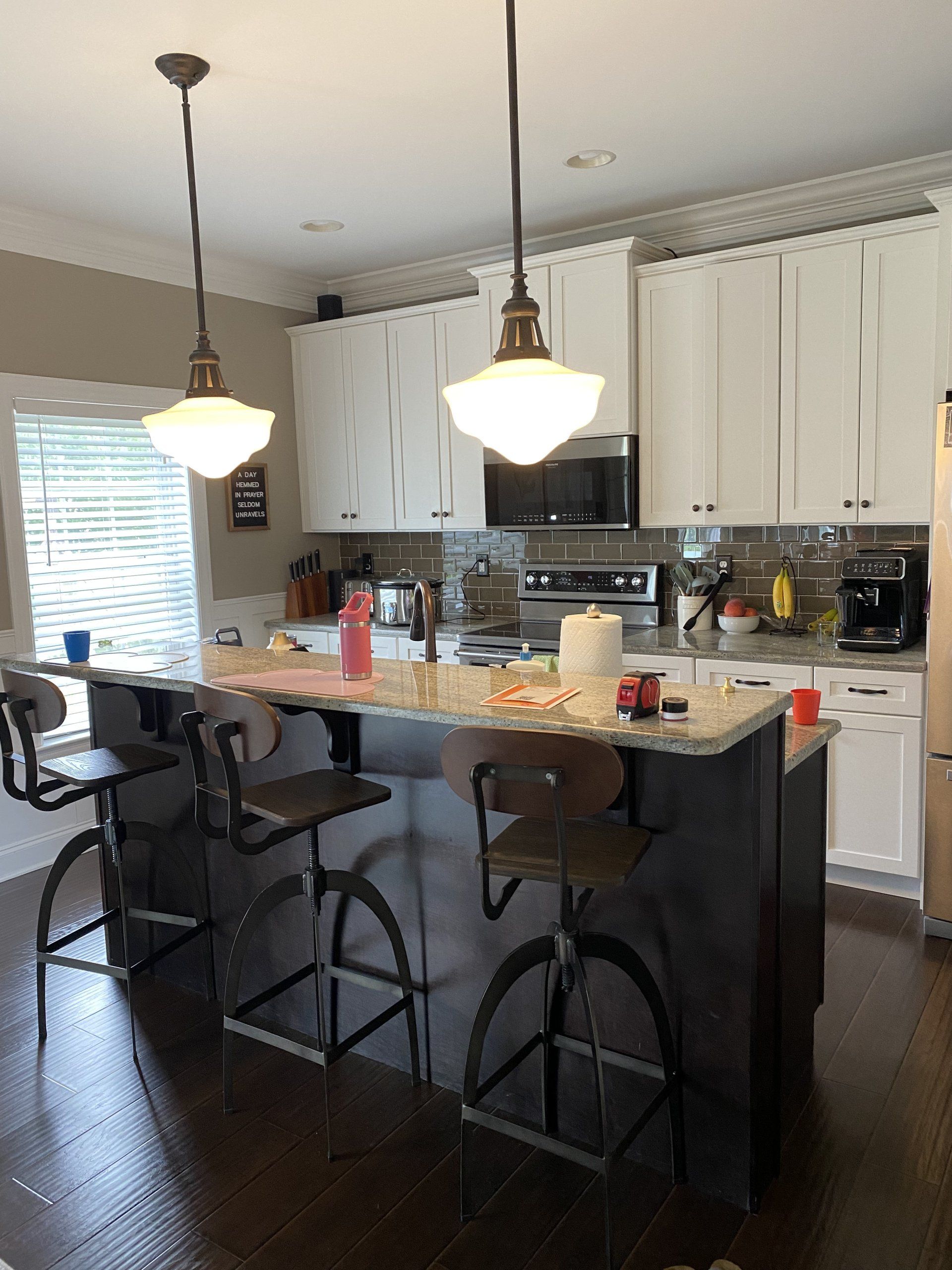 Kitchen with dark island, white cabinets, pendant lights, and bar stools.