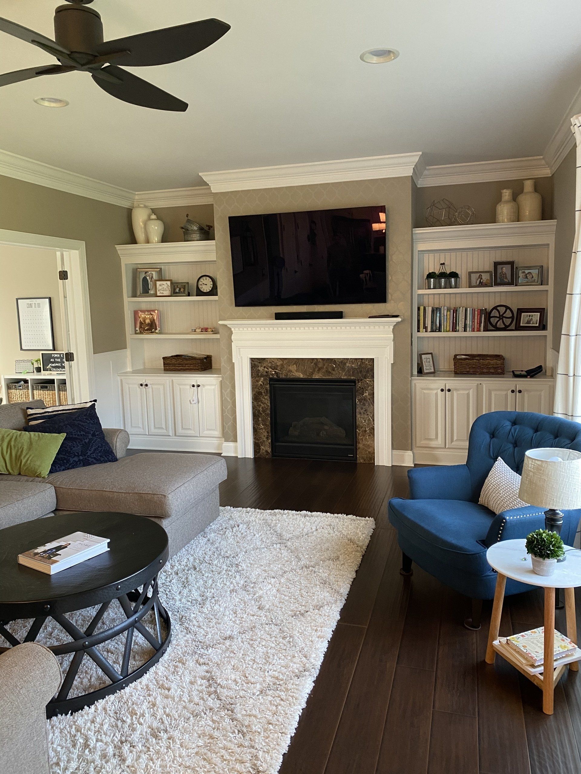 Cozy living room with fireplace, wall-mounted TV, gray sofa, blue chairs, and built-in shelves