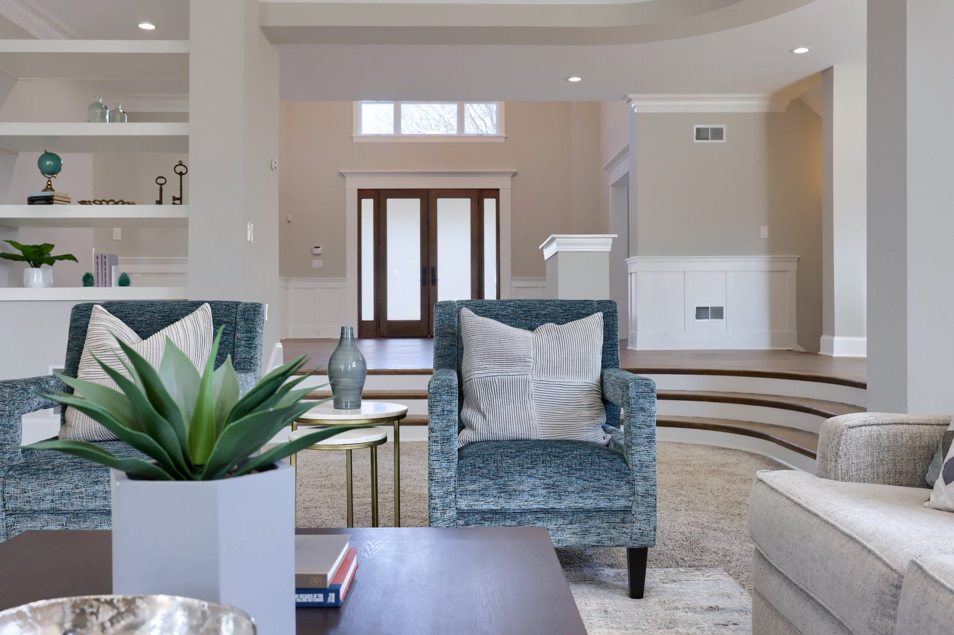Bright modern living room with patterned chairs, beige sofa, plant, and open staircase