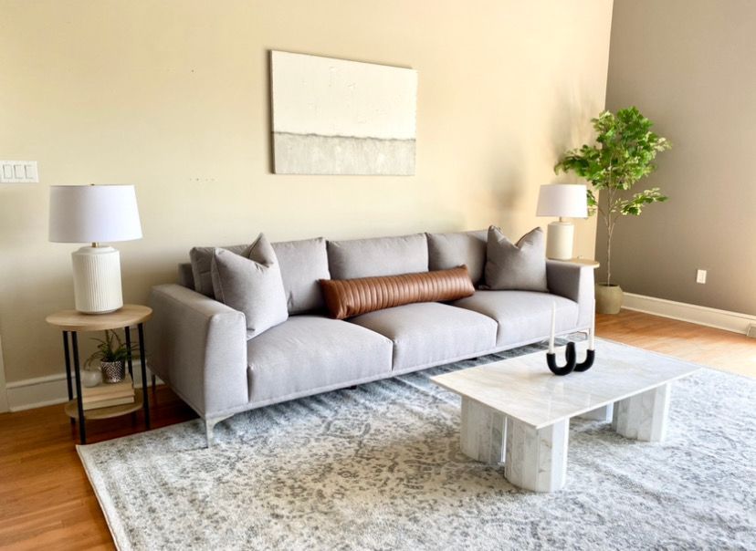 Modern living room with a gray sofa, white coffee table, lamps, plant, and abstract wall art.