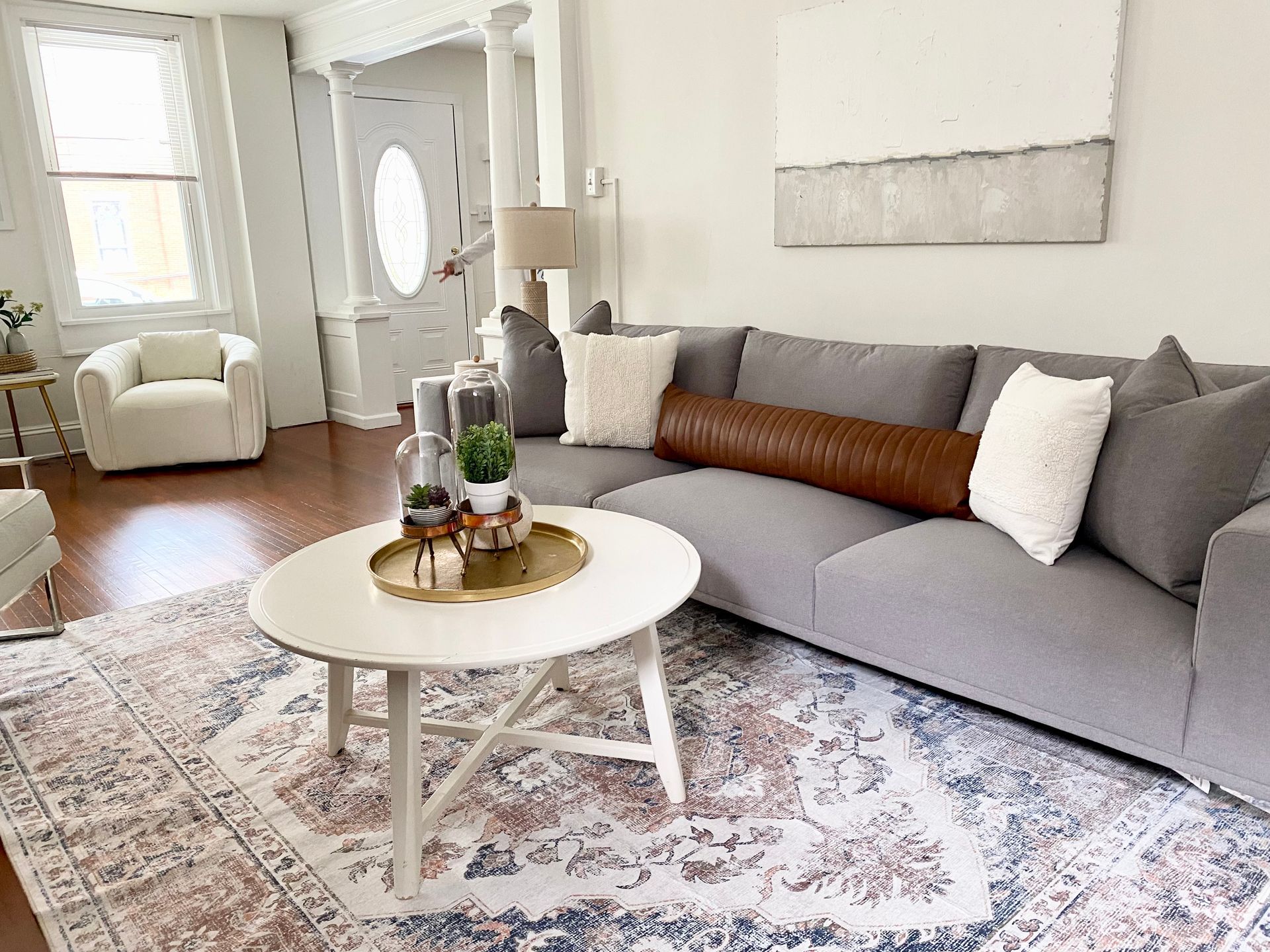 Bright living room with a gray sectional, white coffee table, patterned rug, and front door near a window.