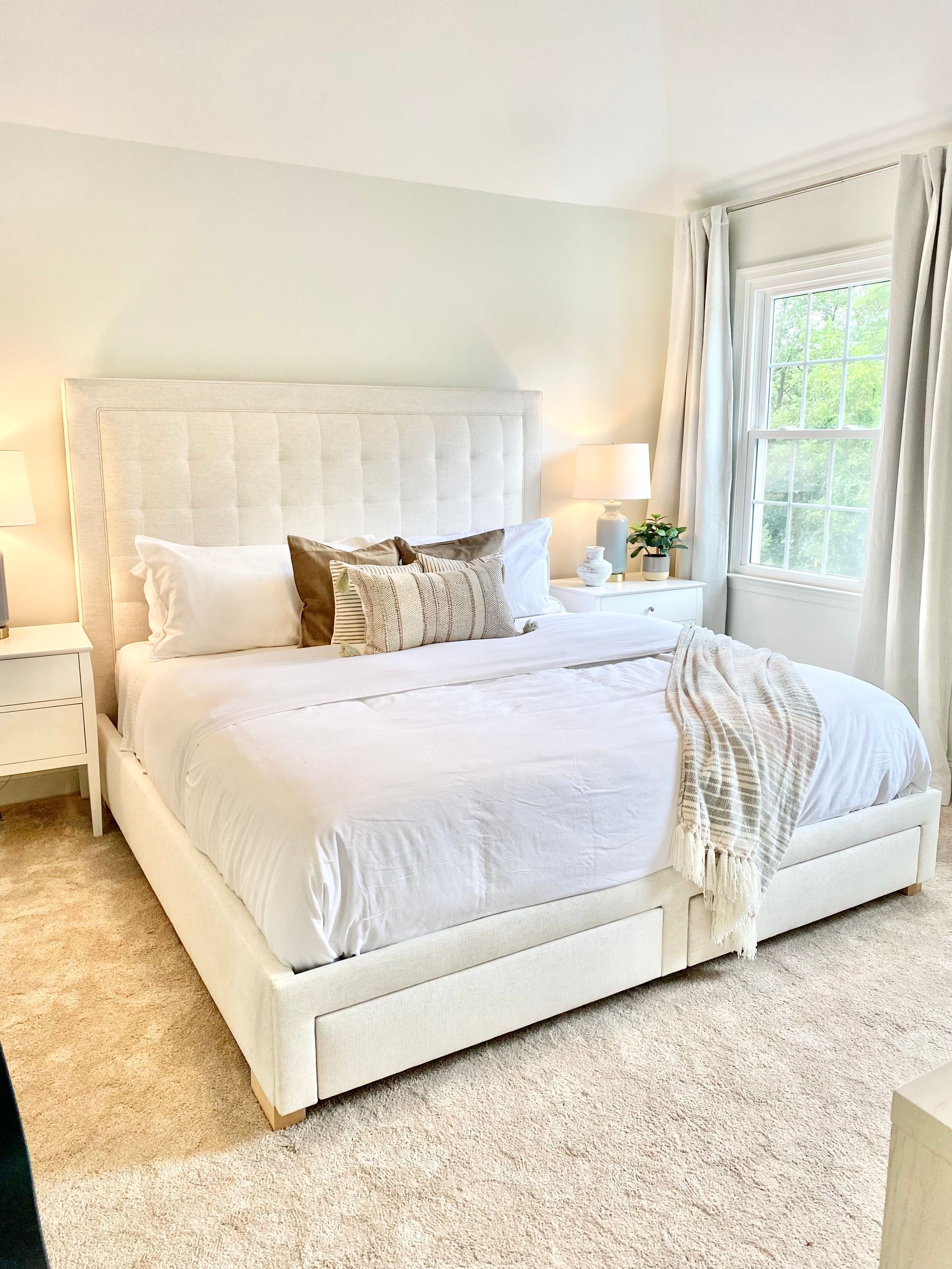Bright bedroom with a white bed, neutral decor, and a large window letting in natural light