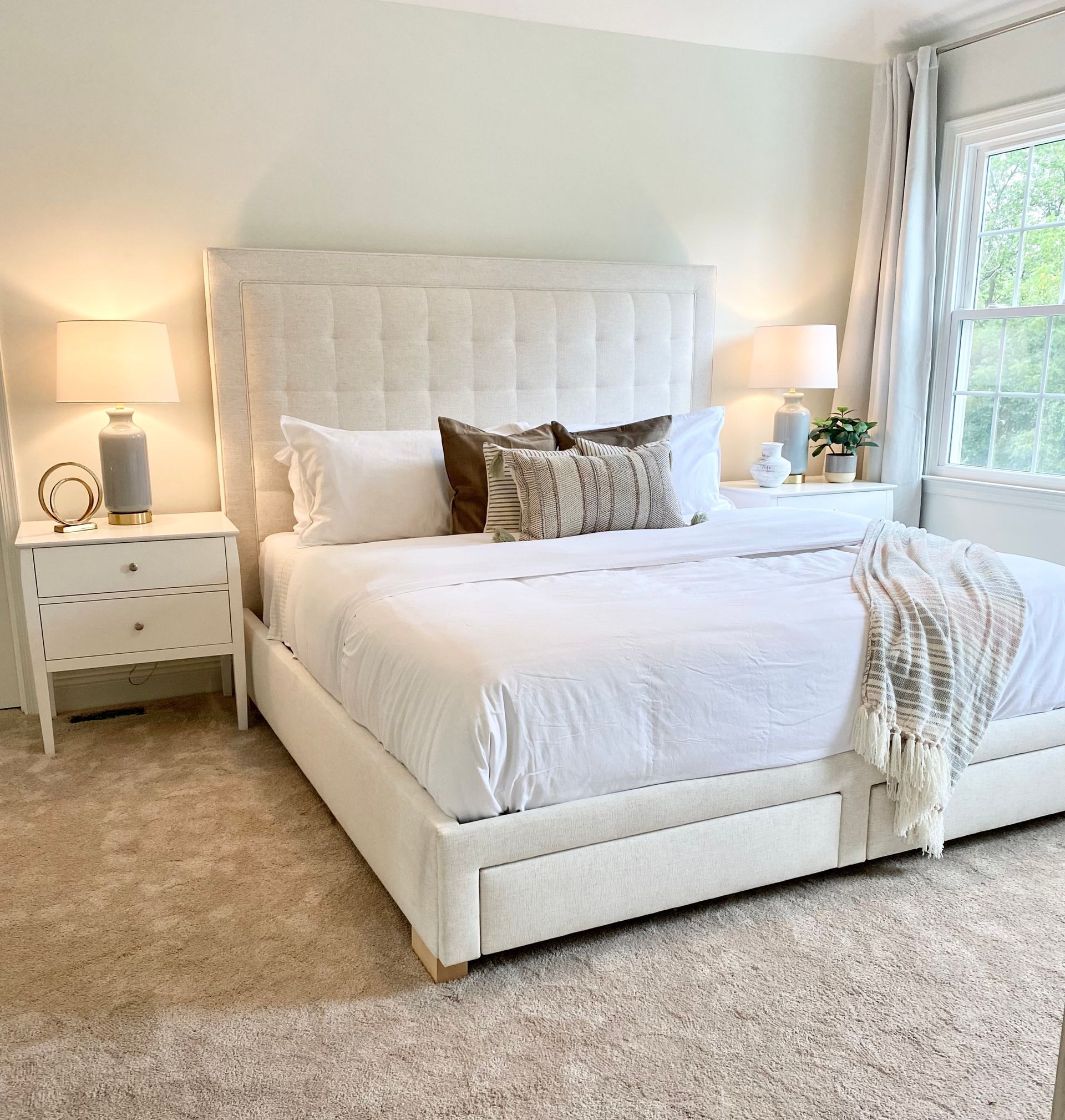 Bright white bedroom with tufted bed, nightstands, lamps, and beige carpet by a window