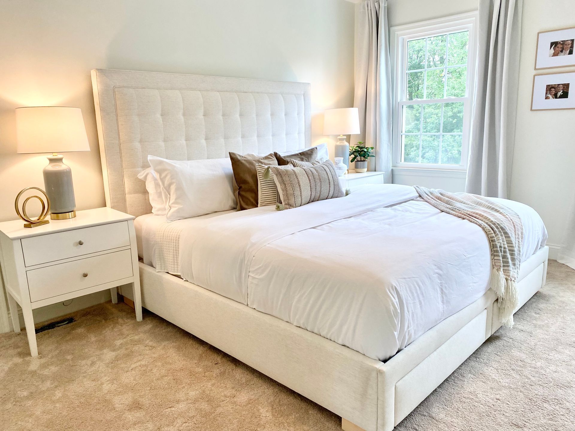 Bright white bedroom with tufted bed, bedside lamp, and sunlit windows