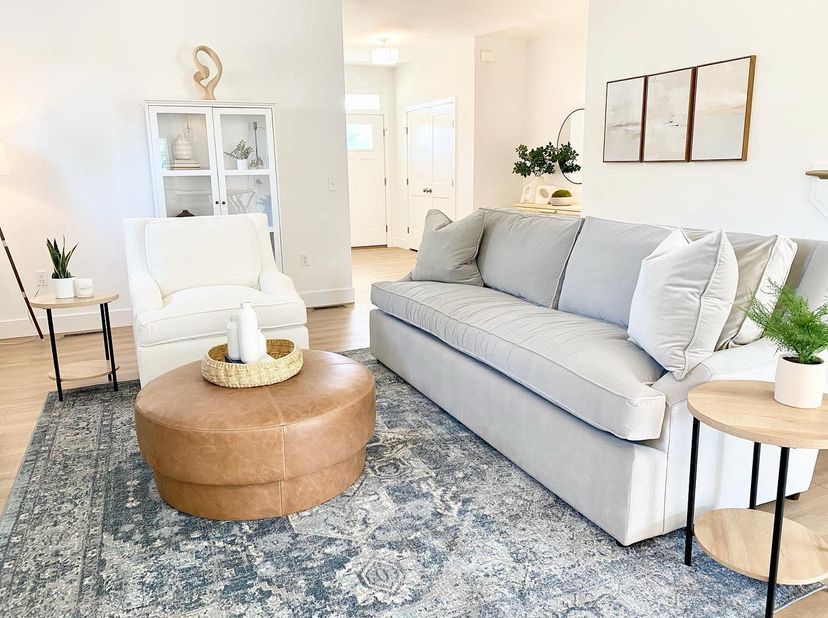 Bright living room with gray sofa, white chair, round tan coffee table, and blue patterned rug