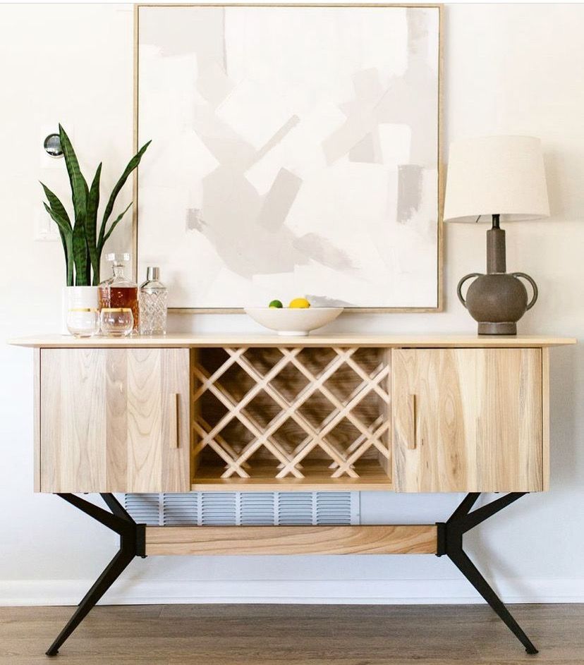 Modern wood console with wine rack, lamp, and plant against a light wall.