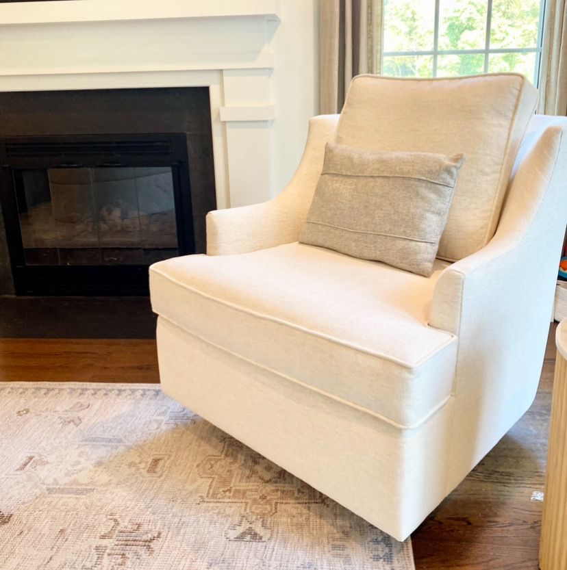 Cream upholstered armchair beside a white fireplace on a patterned rug in a bright living room