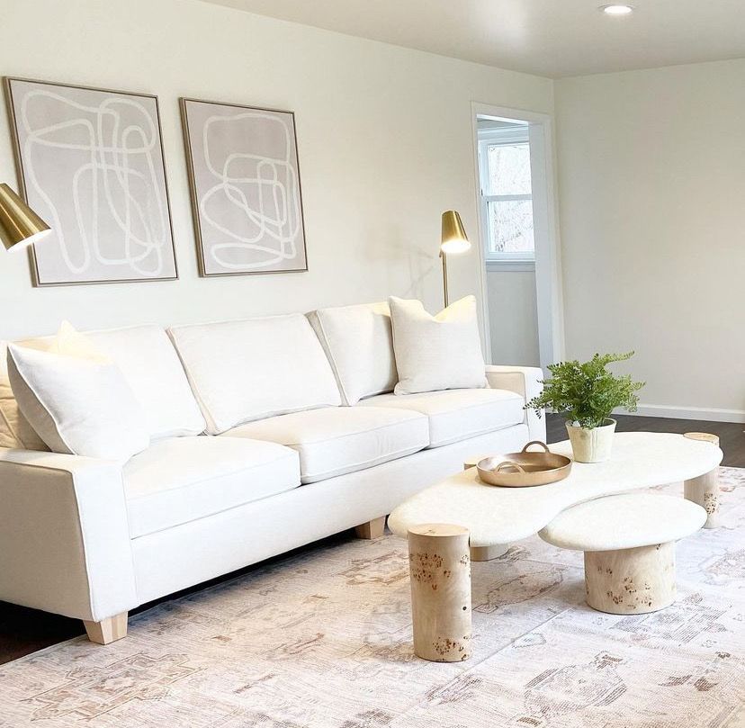 Bright living room with white sofa, abstract wall art, gold lamps, and round marble coffee tables