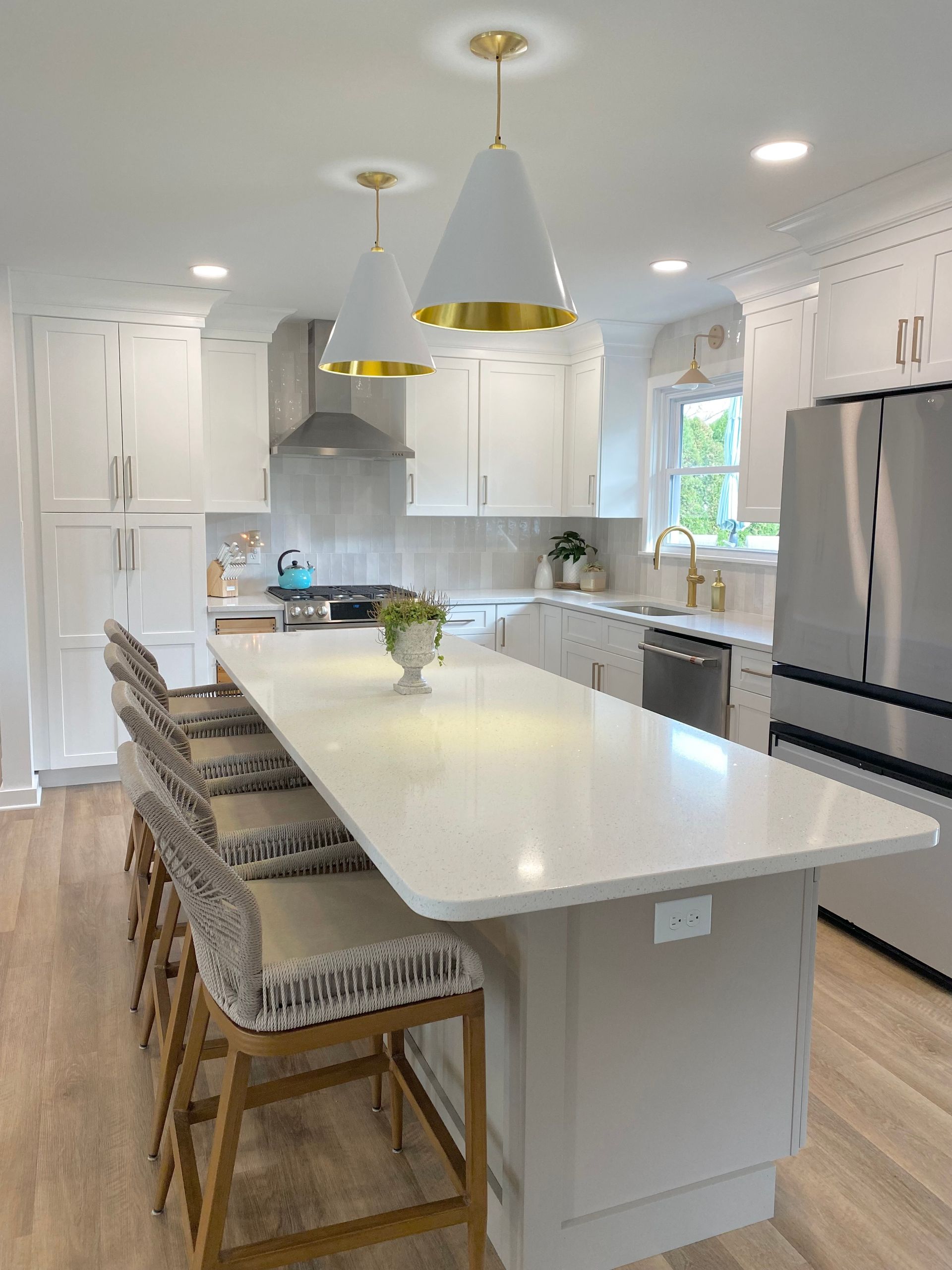 a kitchen with white cabinets , stainless steel appliances , a large island and stools .