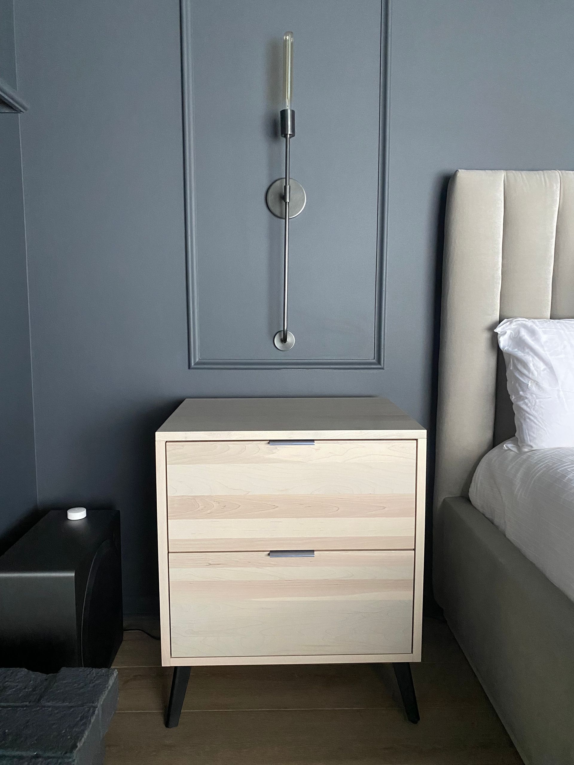 Modern bedroom with light wood nightstand, wall candle sconce, bed, and dark gray walls