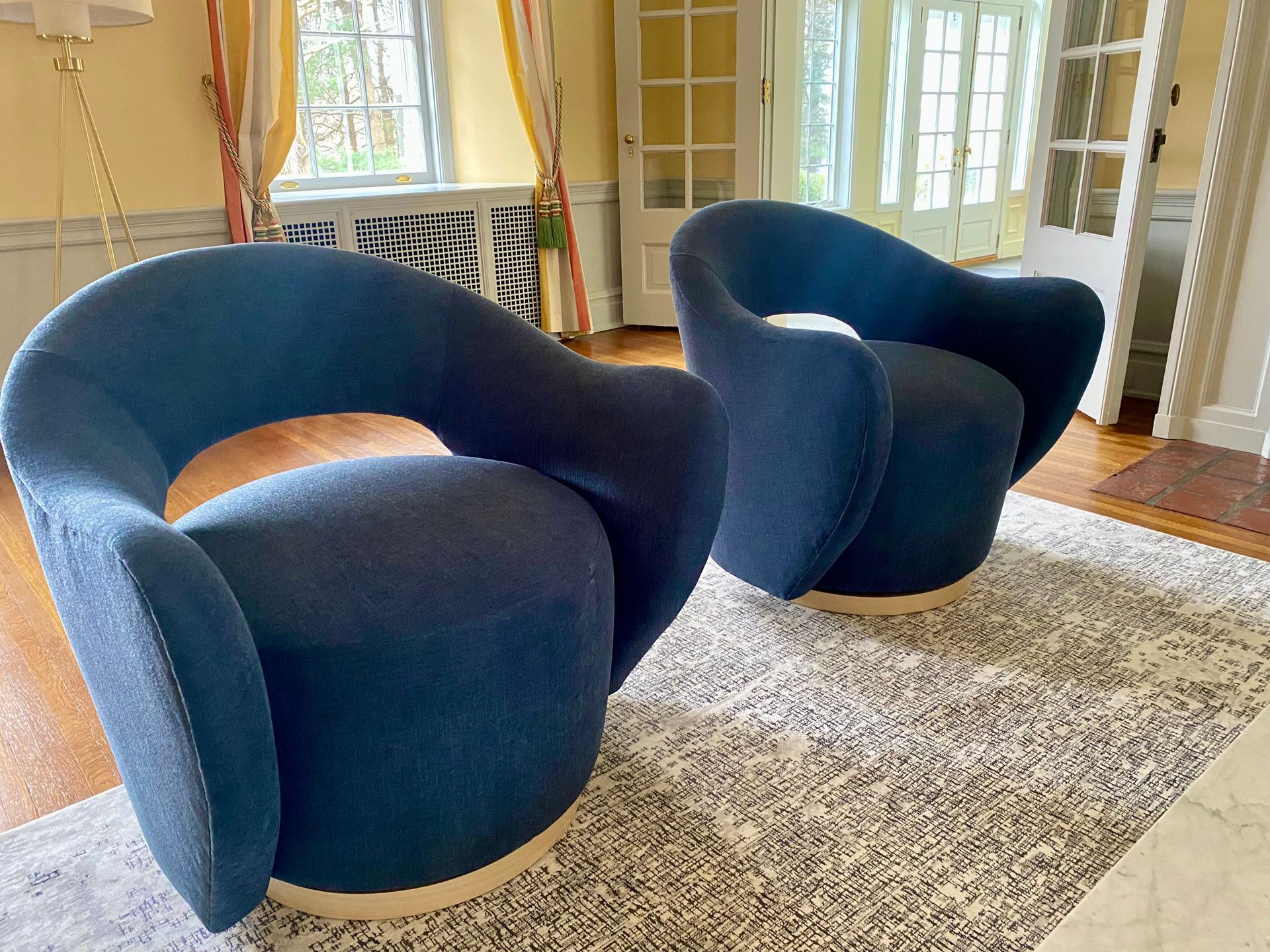 Two navy blue armchairs on a light patterned rug in a sunlit room