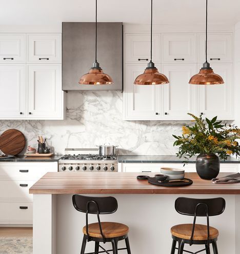 Modern white kitchen with marble backsplash, copper pendant lights, and a wood island with two stools