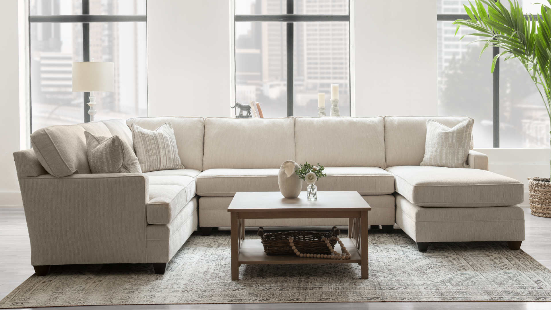 Bright living room with beige sectional sofa, coffee table, rug, and large windows