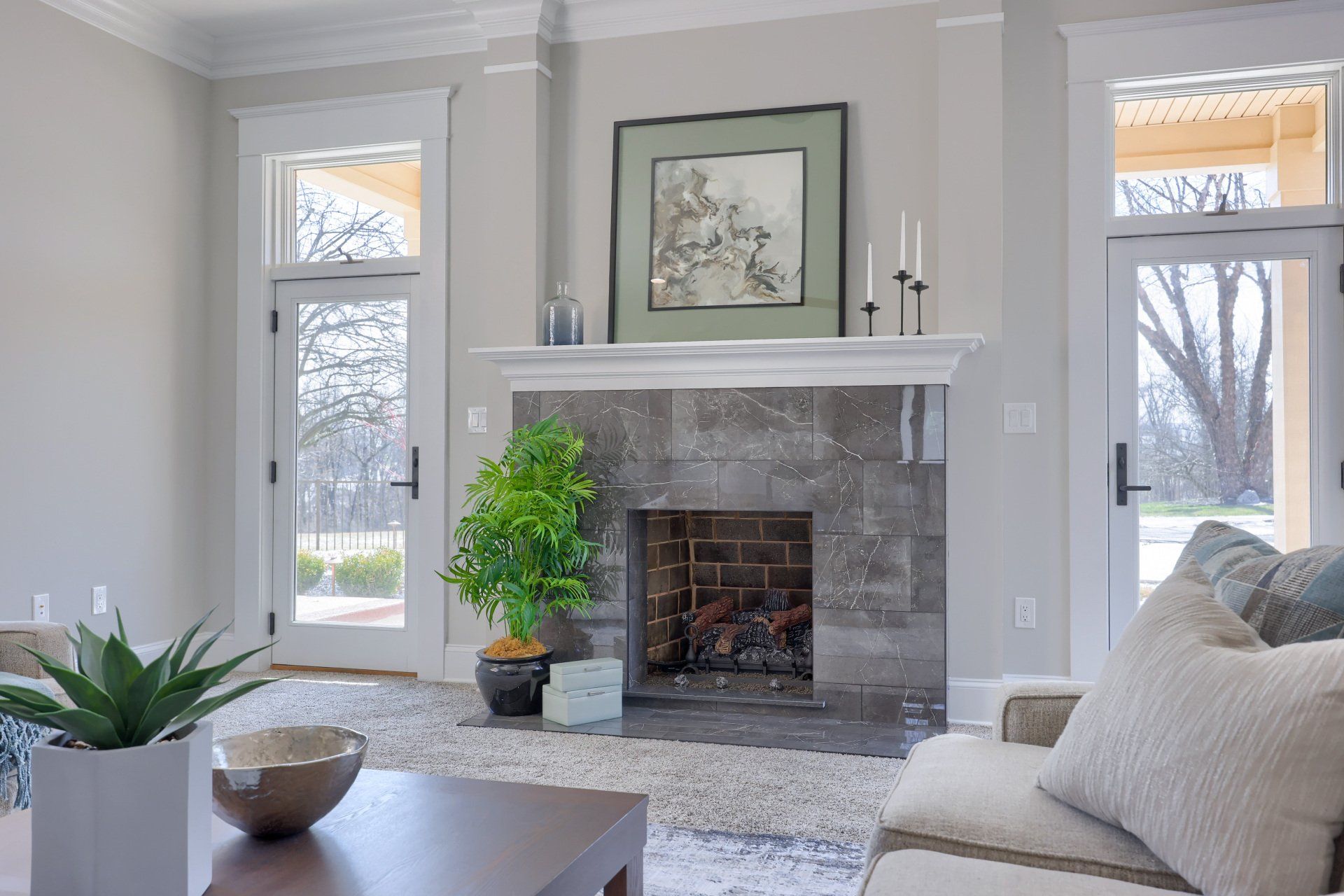 Bright living room with a gray stone fireplace, light walls, large windows, and beige sofa.