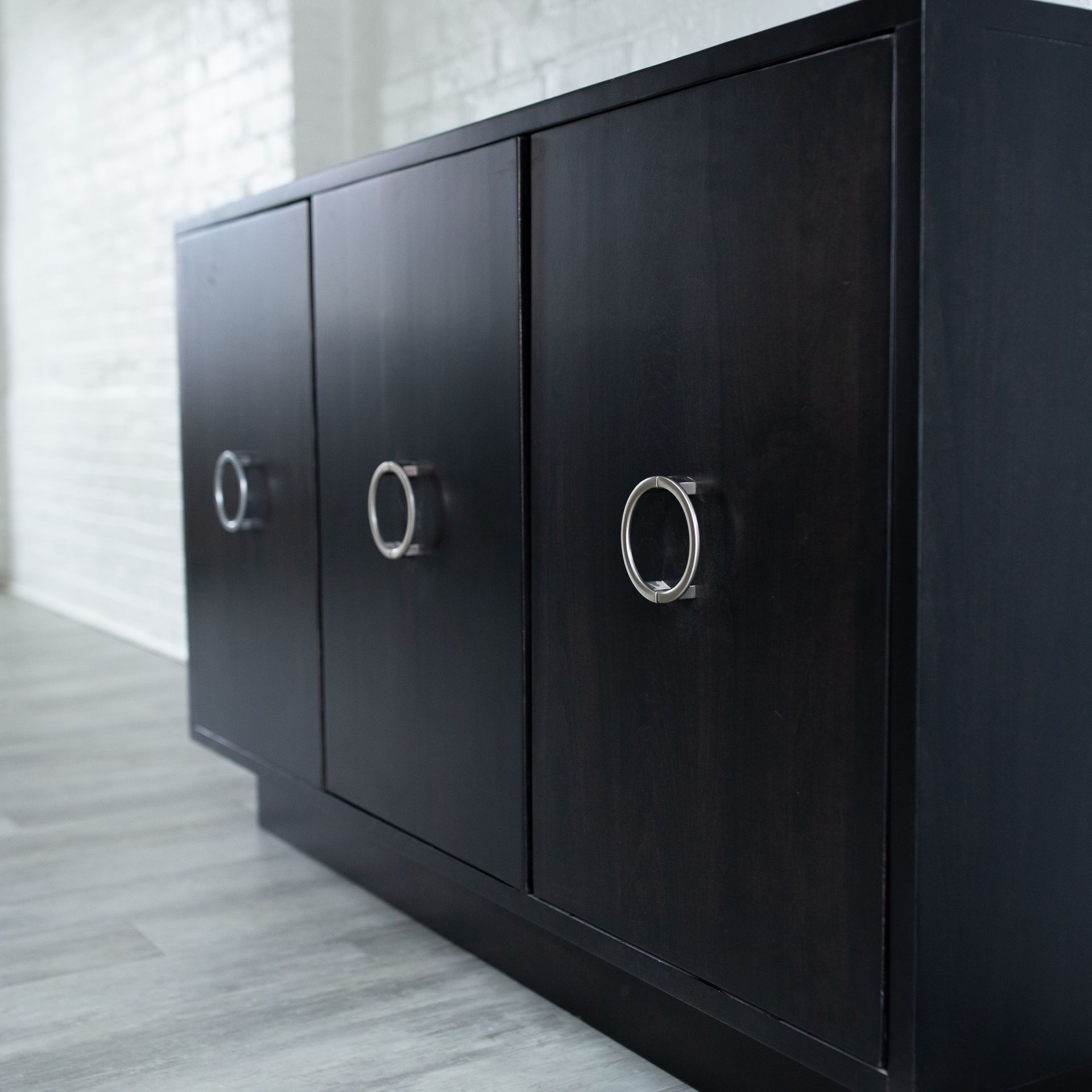 Black cabinet with three silver-ringed doors against a light wall in a modern room