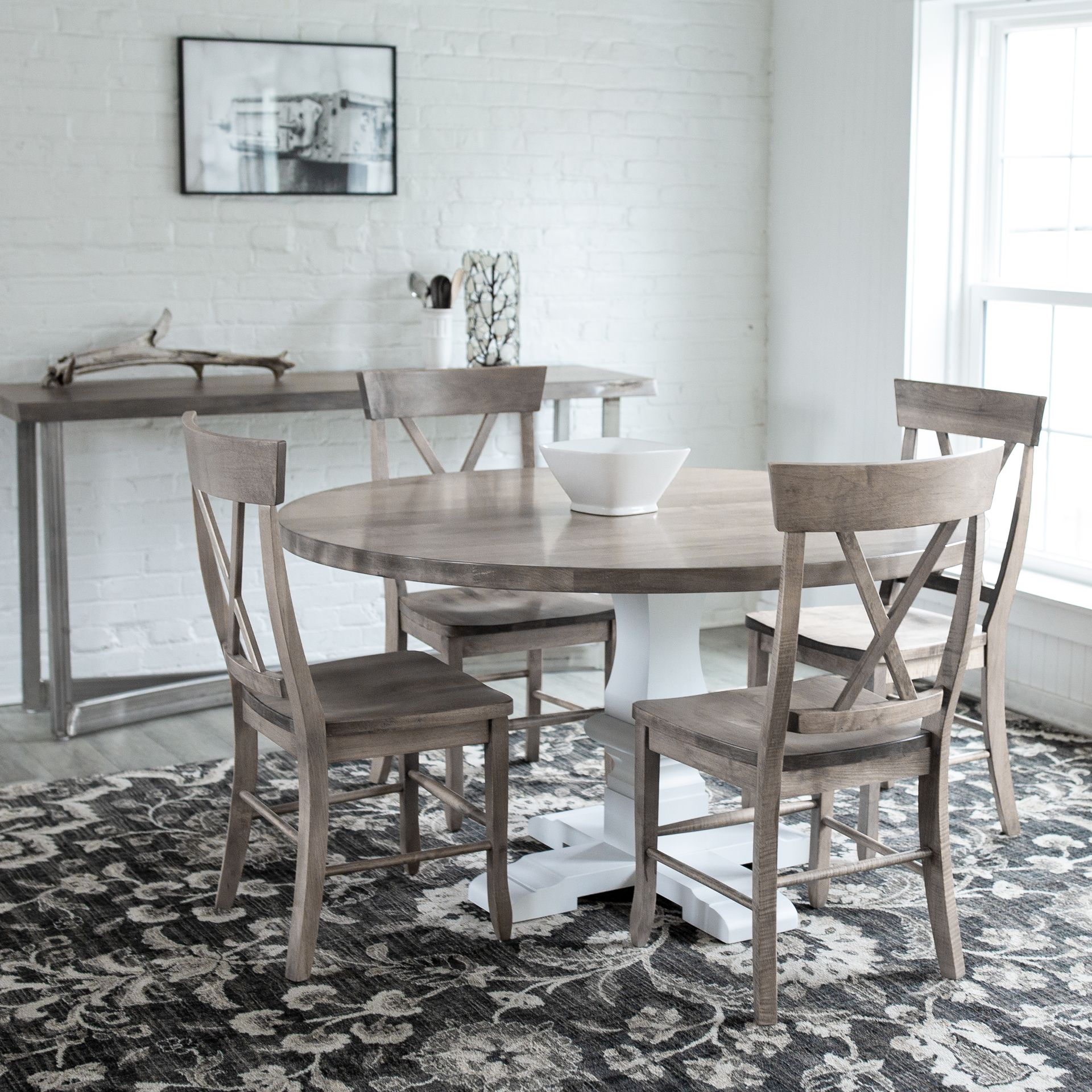 Bright dining room with round wooden table, four chairs, and a sideboard against a white brick wall.