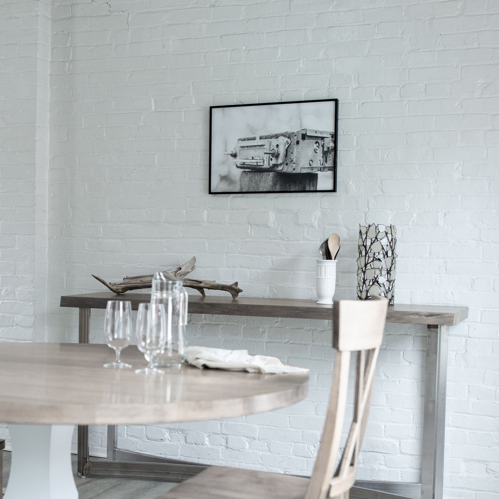 Minimalist dining room with a round table, white brick wall, and framed black-and-white art.