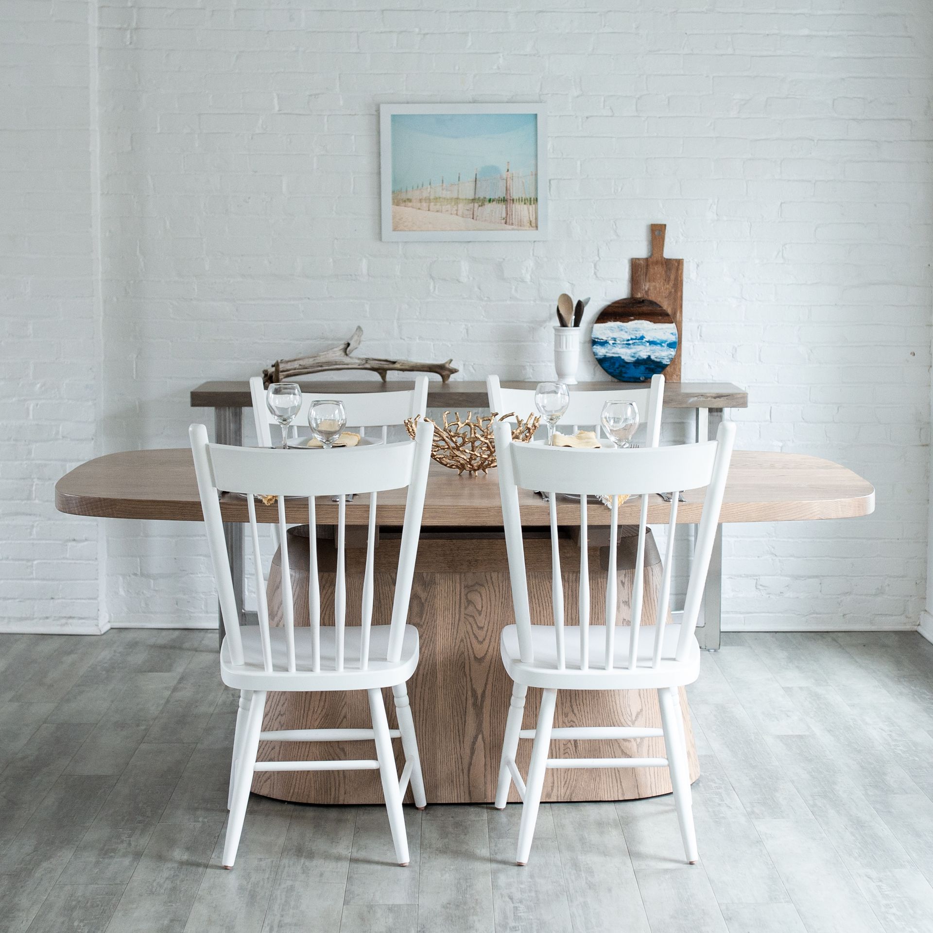 Bright dining room with white chairs, rustic wood table, and beach-themed decor on a white brick wall.