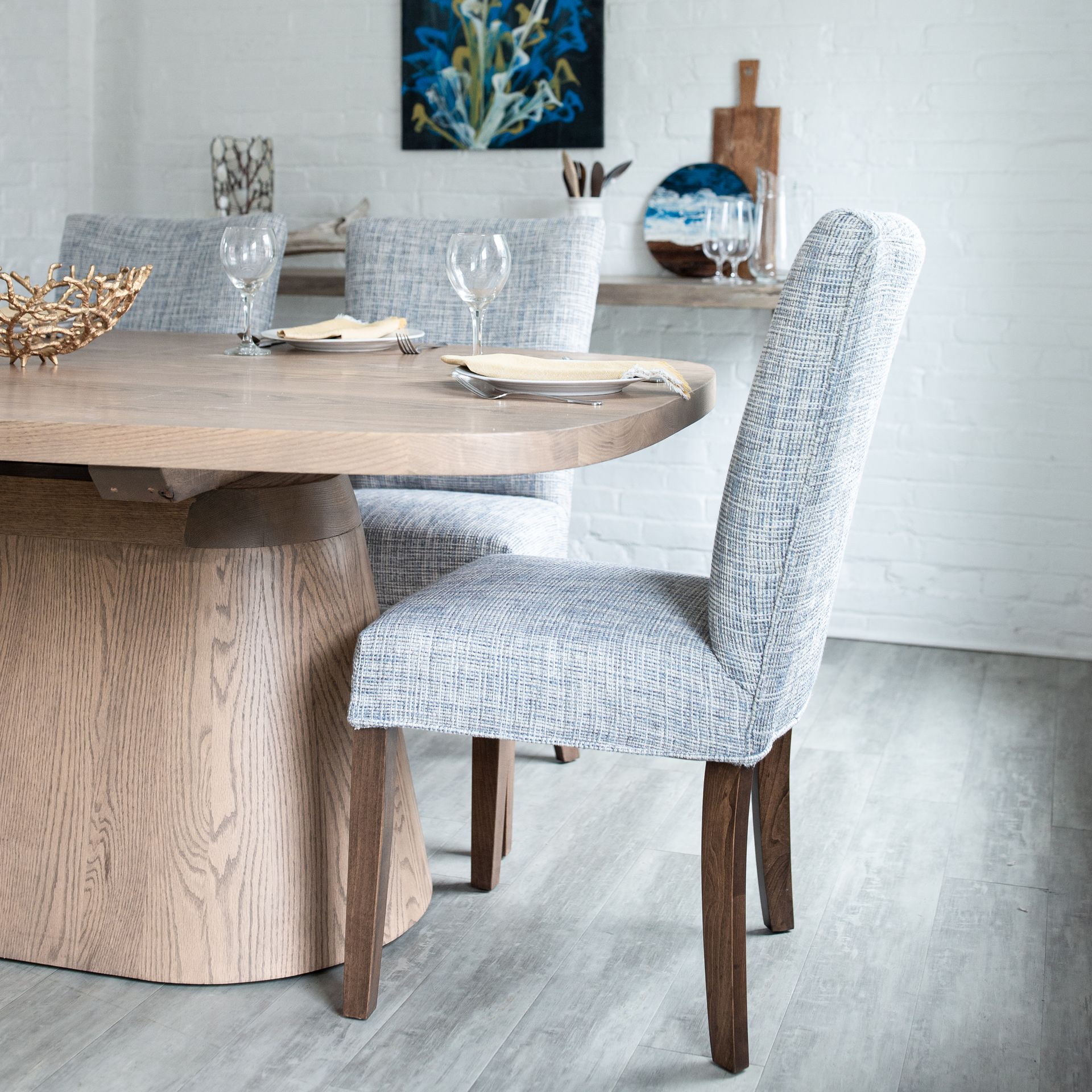 Modern dining room with a round wooden table and upholstered gray chairs on a light floor.
