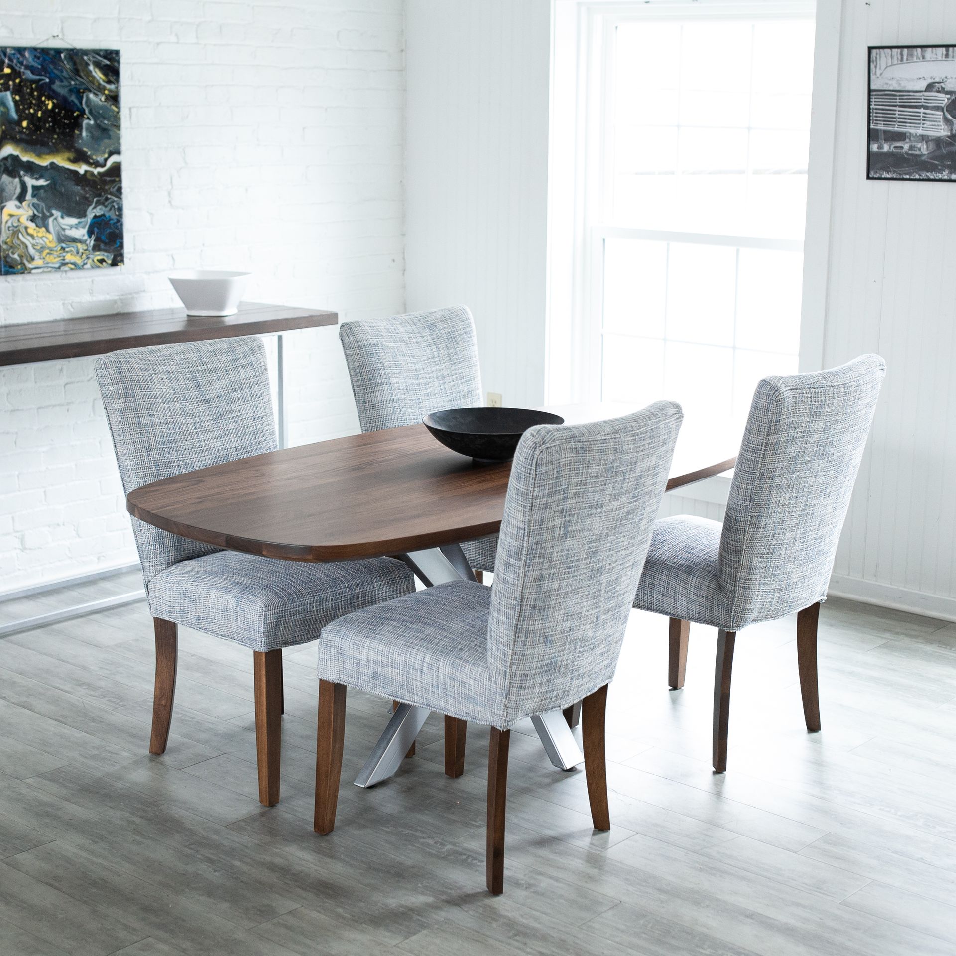 Modern dining room with a wooden table, four gray upholstered chairs, and a bright white interior