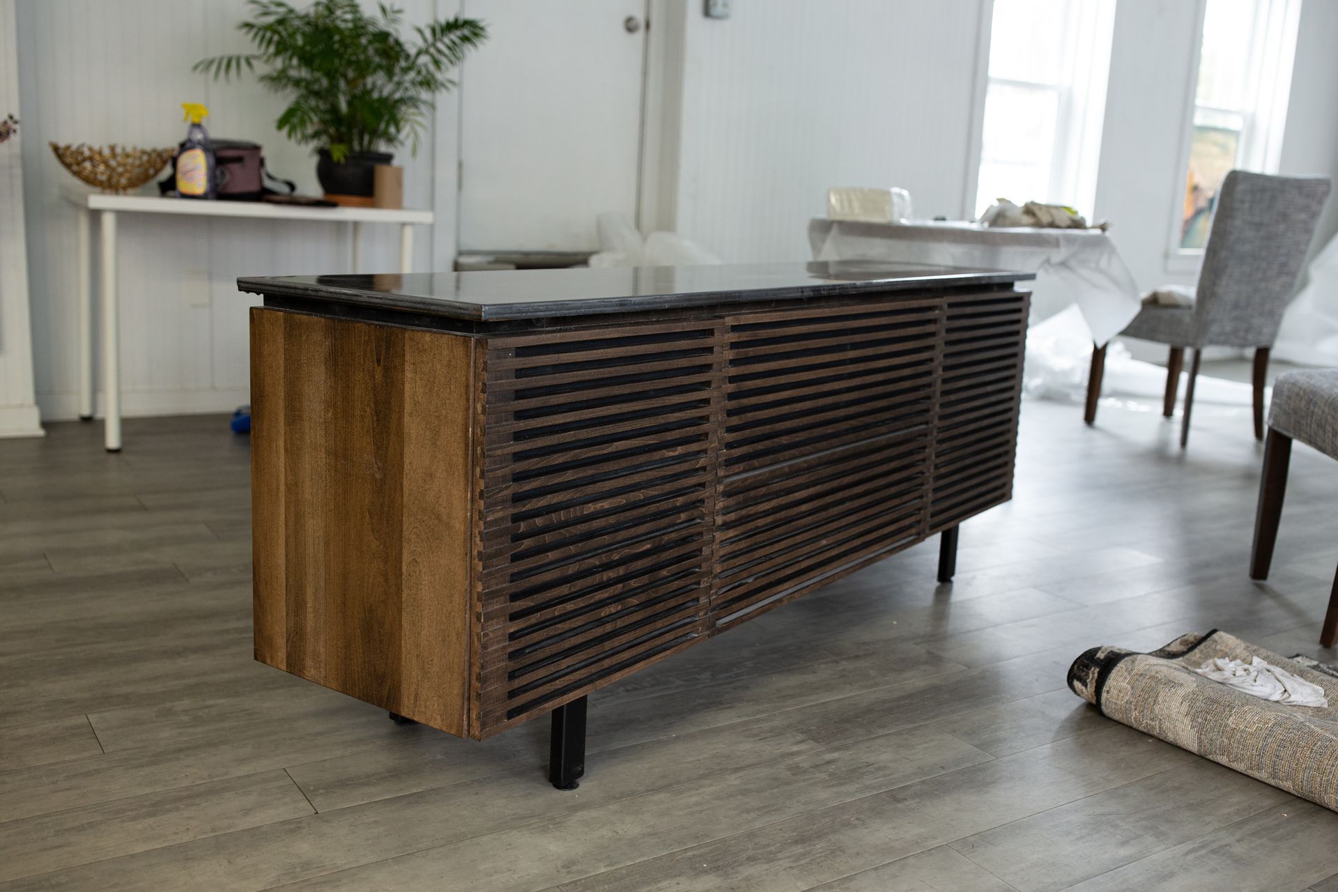 Wood-and-black slatted kitchen island in a bright room with tables, chairs, and a potted plant