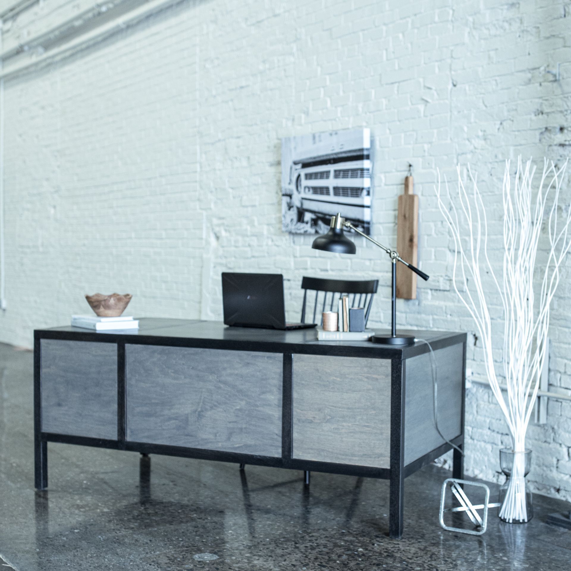 Modern desk with laptop and lamp against a white brick wall in a minimalist office room
