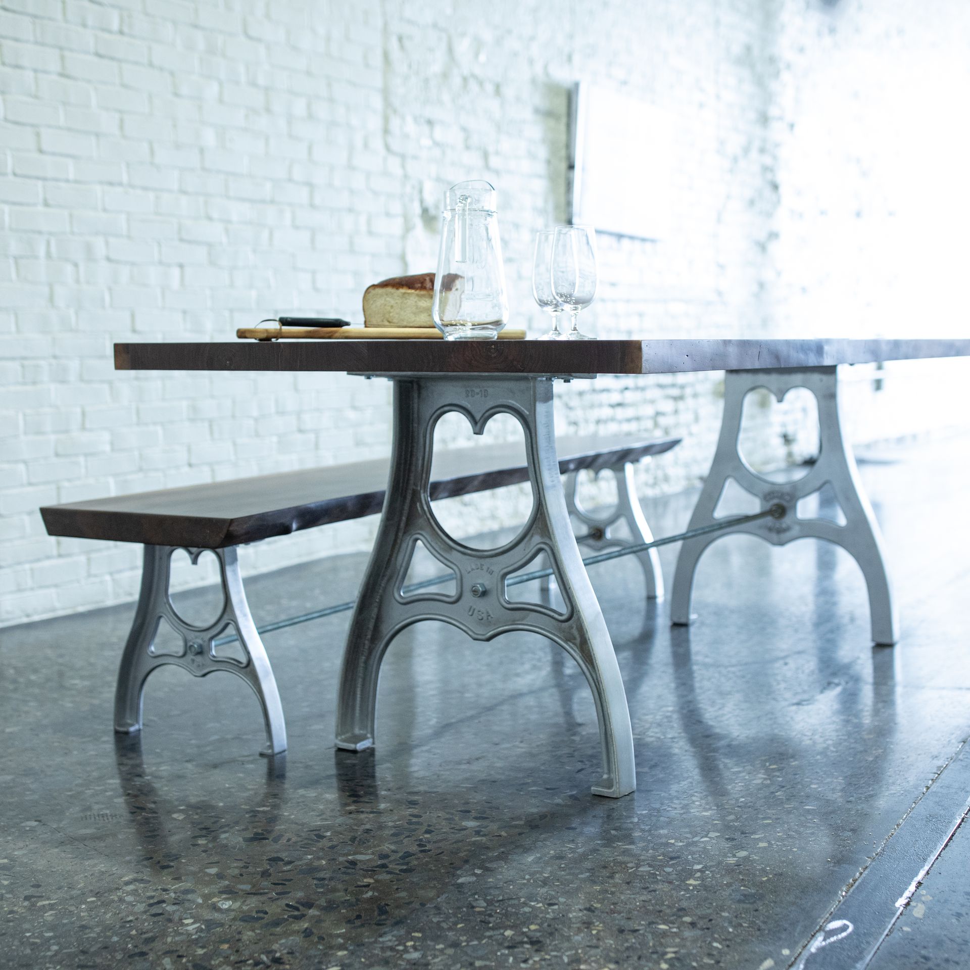 Rustic wooden table with metal benches in a bright, minimalist cafe against a white brick wall