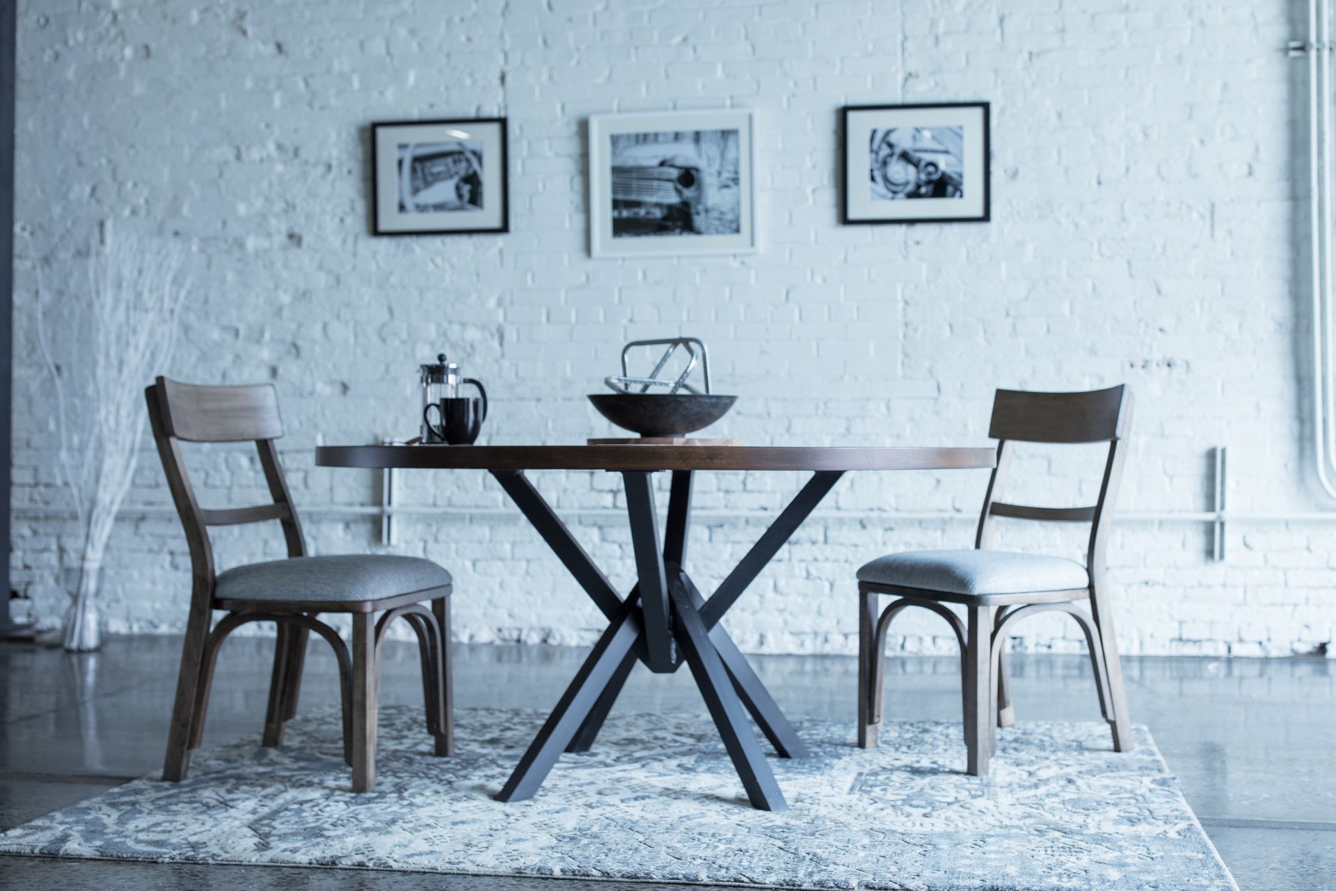 Small dining nook with two wooden chairs, round table, wall art, and a light rug on a white wall backdrop