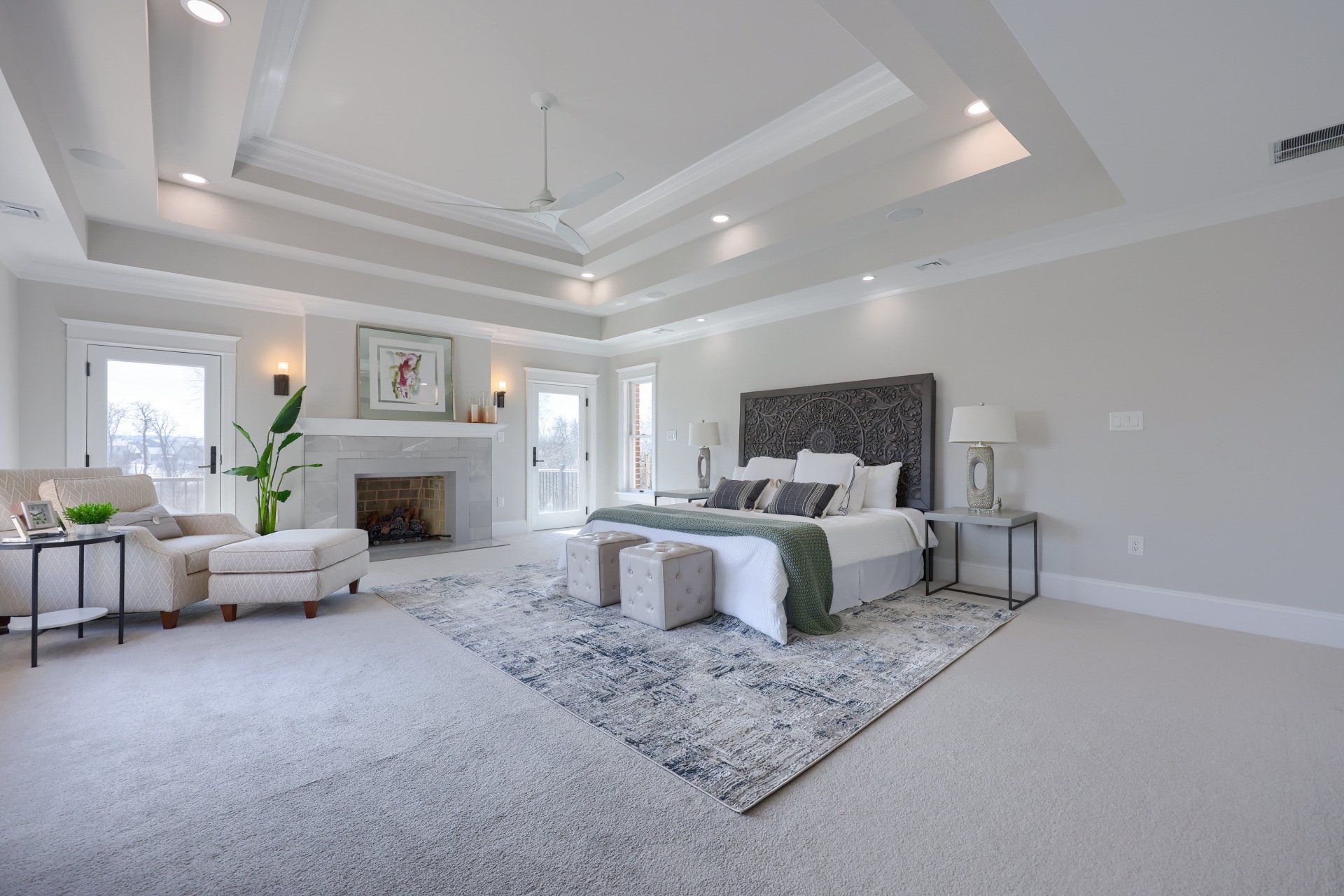 Spacious white bedroom with tufted bed, fireplace, seating area, and large windows