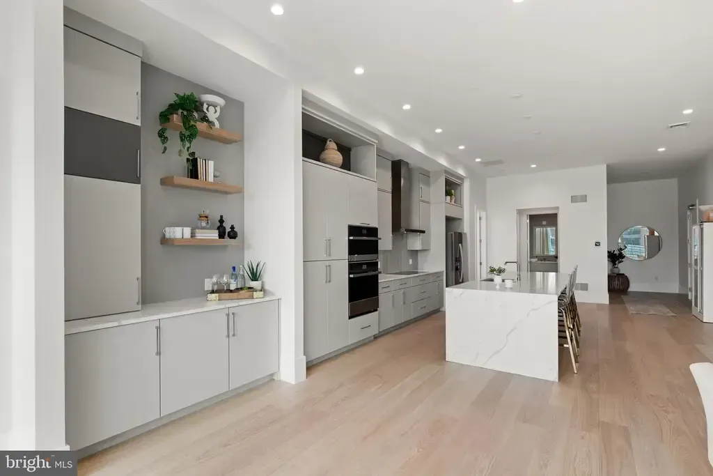 Bright modern open-plan kitchen and living room with white cabinets, wood floors, and recessed lighting