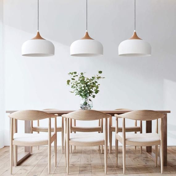 Minimalist dining room with wooden table, four chairs, and three white pendant lights above a small vase centerpiece.