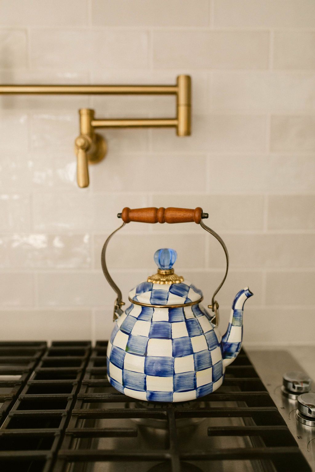 Blue-and-white checkered teapot on a stovetop against a tiled kitchen wall