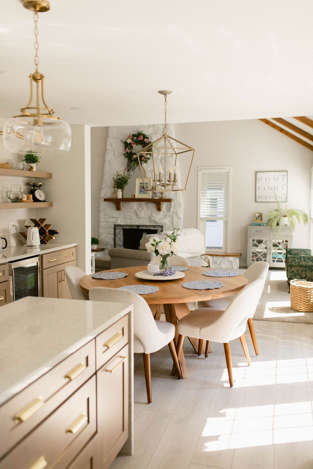 Bright, airy dining room with round wooden table, white chairs, and gold-accented kitchen island