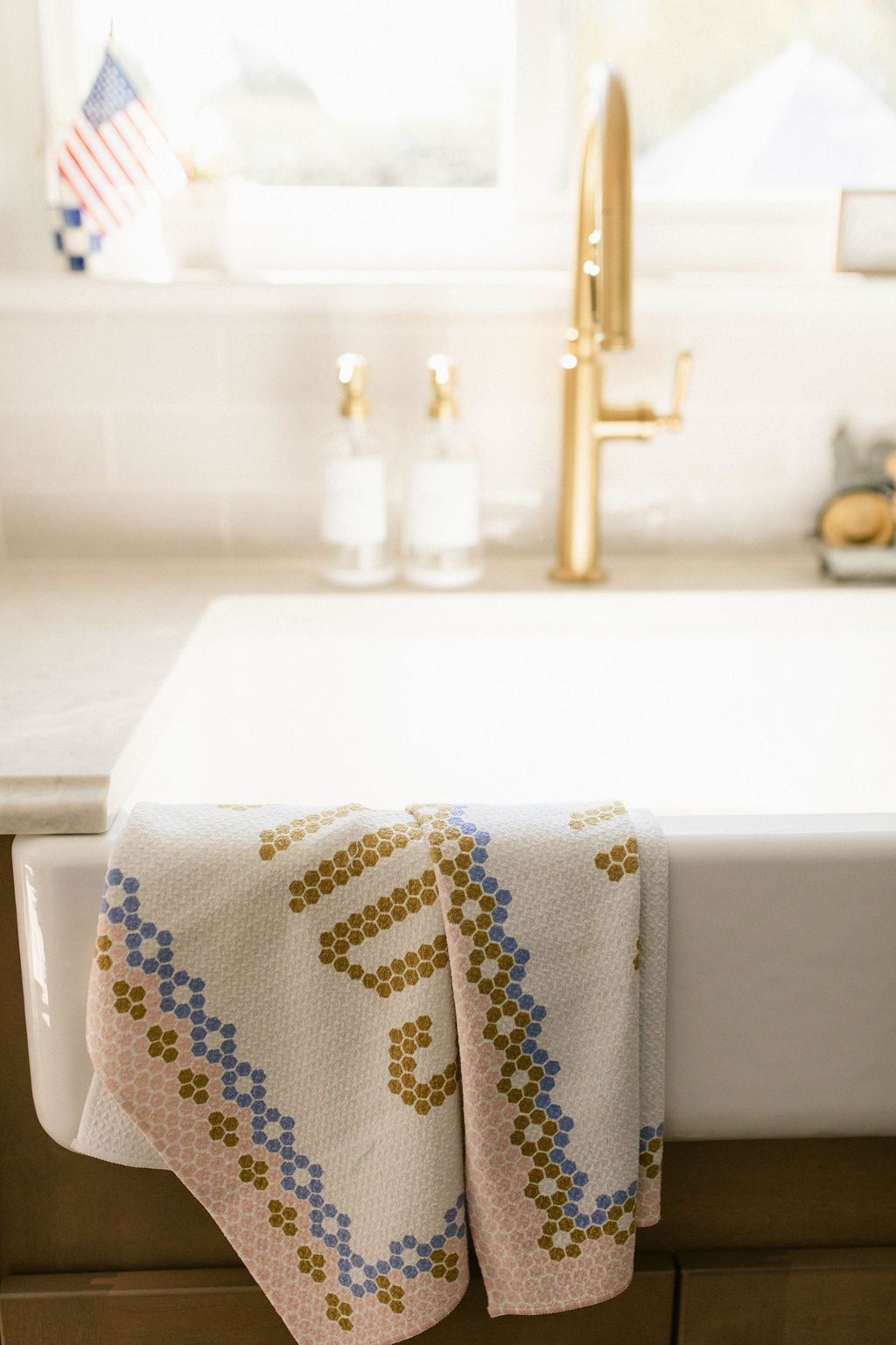 White bathroom sink with gold faucet and a patterned towel draped over the front.
