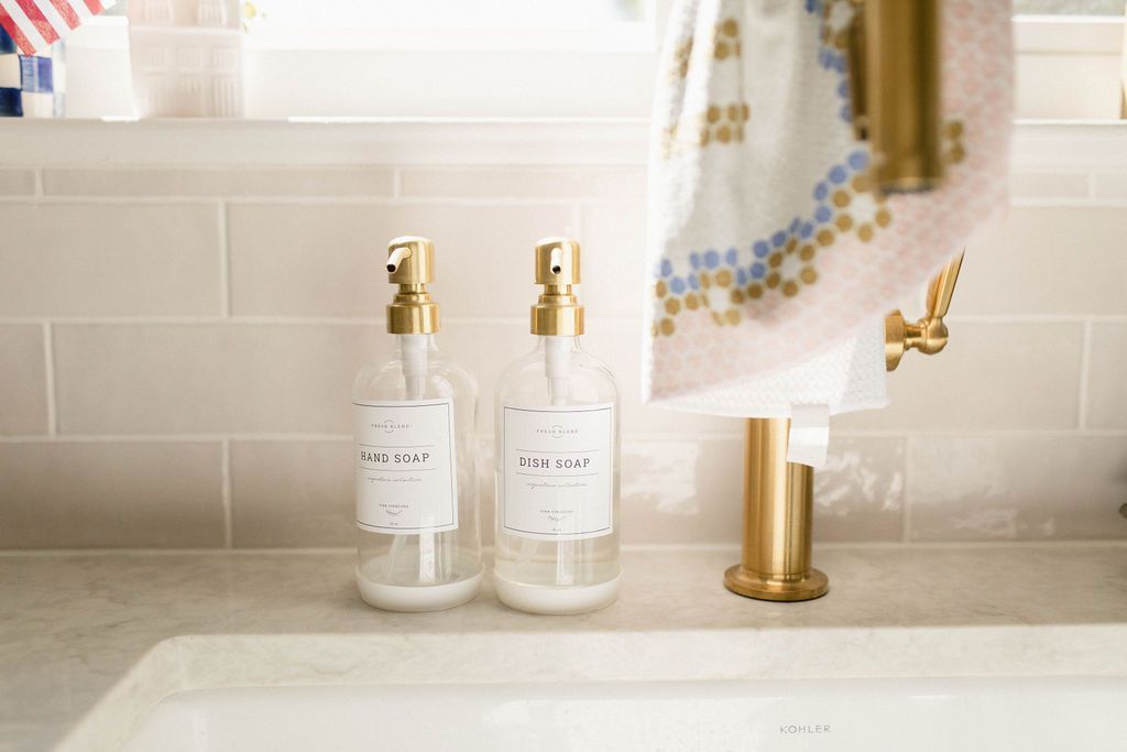 Two gold soap dispensers on a bathroom sink beside a hanging hand towel