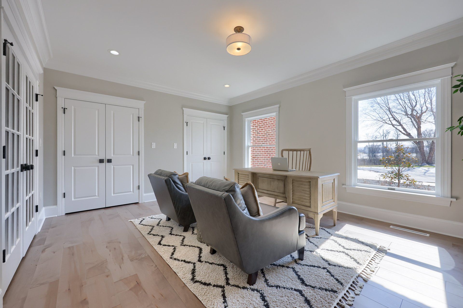 Bright living room with gray chairs, patterned rug, desk, and large windows.