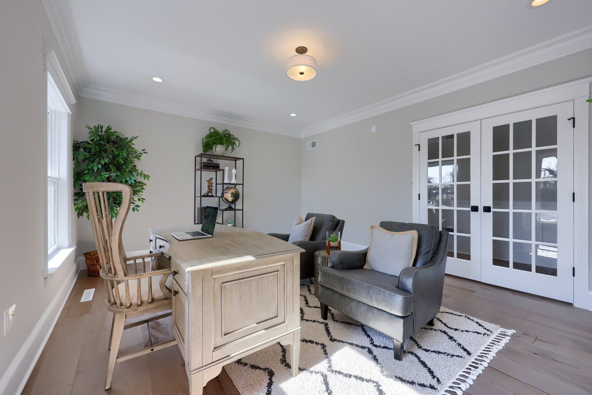 Bright living room with gray sofa, light wood table, chair, plants, and French doors