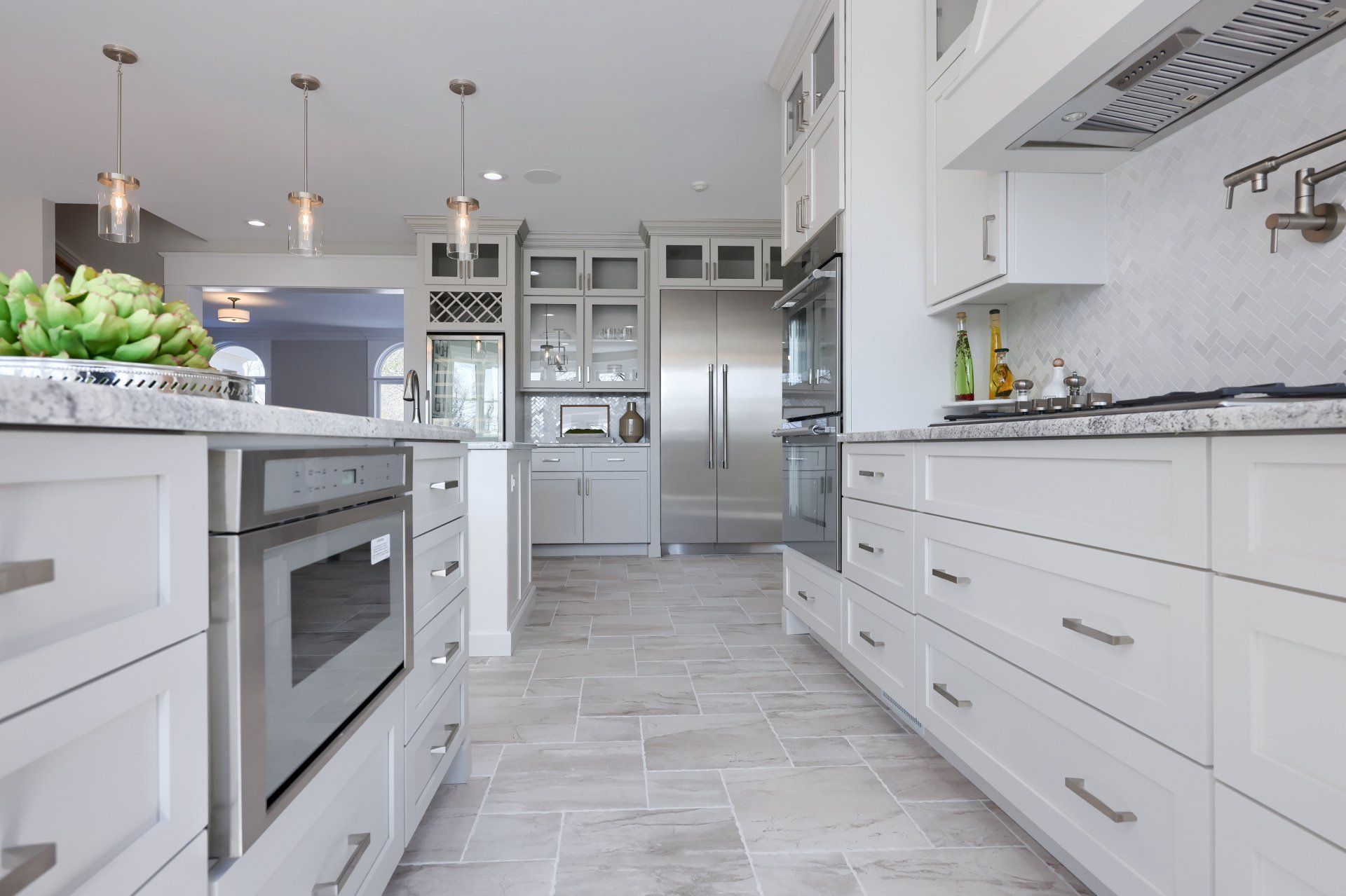 Bright white modern kitchen with gray tile floor, island, stainless appliances, and large windows