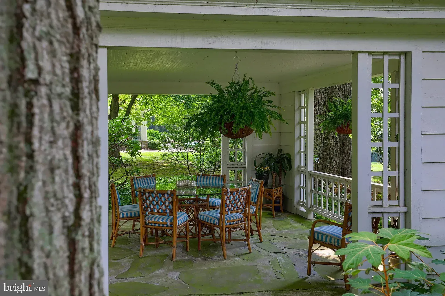 Covered porch with wooden dining set, hanging plants, and garden view through open railings.